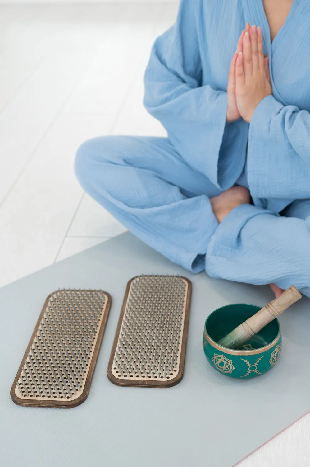 Asiatische Frau sitzt auf einer Yogamatte mit tibetischer Klangschale und Sadhu-Brettern.